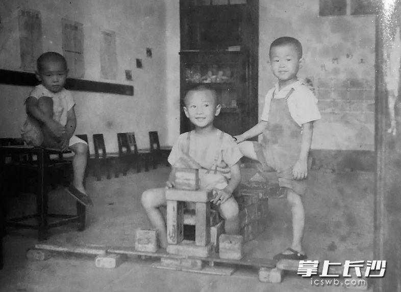 1951年,时值抗美援朝,长沙一家幼儿园内,三个孩子用自己的双手做成一架“战斗机”,中间的孩子代表战斗机驾驶员。